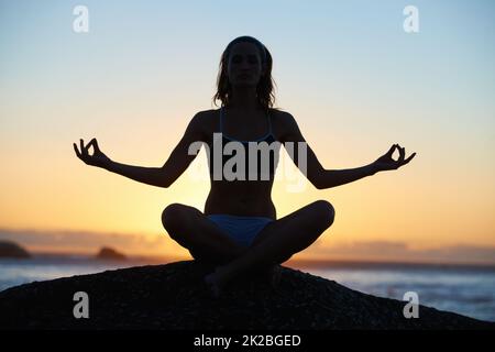 In contatto con la natura. Silhouette di una giovane donna che fa una posa yoga contro un tramonto arancione. Foto Stock