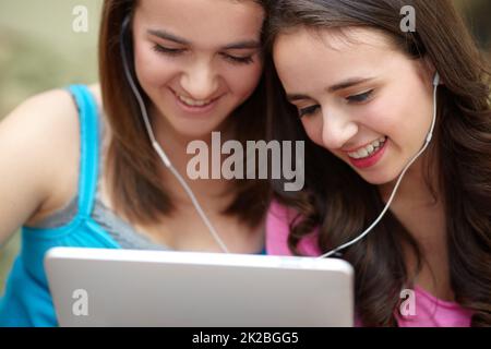 Condividiamo tutto. Due ragazze adolescenti condividono le cuffie mentre osservano un tablet. Foto Stock