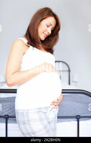 Tenendolo al suo grumo di gioia. Giovane donna felice in piedi nel suo bedrooom mentre lei tiene il suo ventre incinta. Foto Stock