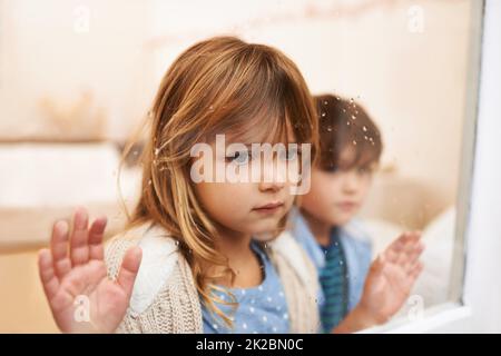 Intrappolato in una scatola di vetro di emozione. Scatto di due bambini infelici che guardano fuori una finestra in una giornata piovosa. Foto Stock