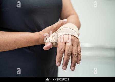 Donna asiatica di mezza età usa bendaggio elastico per curare la sindrome di De Quervain a portata di mano e dito in ufficio. Foto Stock