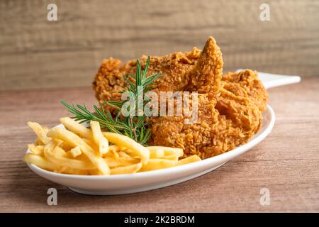 Pollo fritto e patata con foglia di rosmarino, cibo spazzatura ad alto contenuto calorico servito su piatto bianco Foto Stock