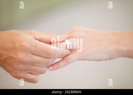 Trovare quello giusto - matrimonio e impegno. Vista ritagliata di una mano di uomo che fa scorrere un anello di nozze su un dito anello di donna. Foto Stock