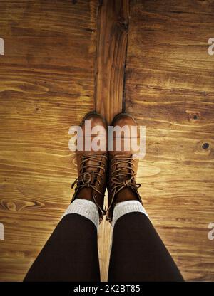Stile rustico. Colpo di POV di una persona che indossa stivali in piedi su un pavimento di legno. Foto Stock