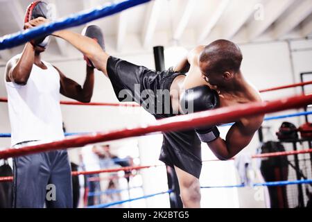 Lanciare un magnifico calcio. Un kickboxer che lancia un calcio forte ai suoi guanti sparring partner. Foto Stock