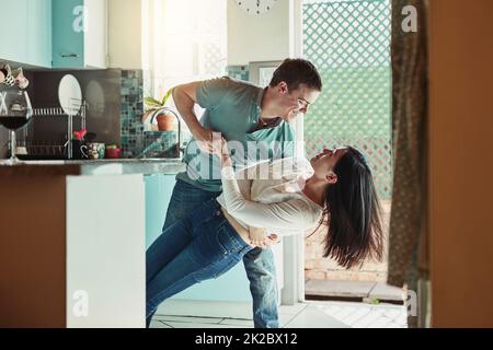 Mi bussa ancora ai piedi. Scatto di una giovane coppia amorevole che balla in cucina. Foto Stock