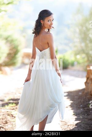 Camminando verso il suo nuovo marito. Ritratto di una giovane donna attraente in un abito da sposa guardando indietro. Foto Stock