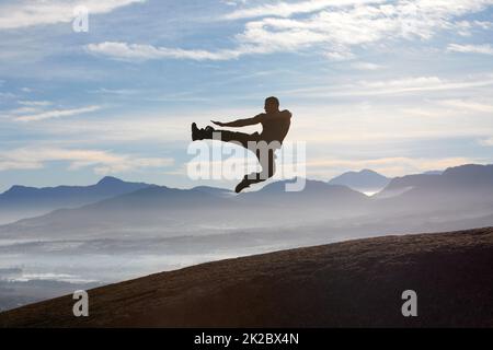 Tecnica di precisione in montagna. Un kickboxer maschio che vola attraverso l'aria mentre pratica la sua tecnica di calcio a mosca. Foto Stock