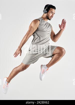 Tutto ciò che serve è tutto ciò che si può ottenere. Studio girato di un giovane sportivo indossando cuffie e saltando su uno sfondo bianco. Foto Stock