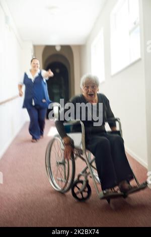 Im spolvero da questo giunto. Sparato di una donna anziana maliziosa utilizzando la sua sedia a rotelle per scappare dalla sua infermiera in una casa di vecchiaia. Foto Stock