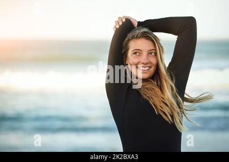 Youve deve essere limber per essere un surfer. Scatto corto di una giovane ragazza attraente surfer che si scalda sulla spiaggia. Foto Stock