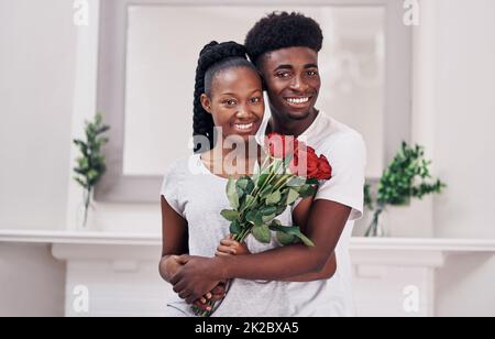 La coppia del premio di anno va a.. Scatto di una giovane donna che tiene un mazzo di rose rosse mentre si alza con il suo ragazzo a casa. Foto Stock