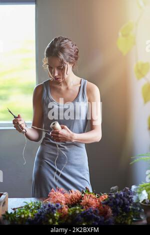 Più idee che tempo. Una giovane donna nel processo di fare una disposizione del fiore. Foto Stock