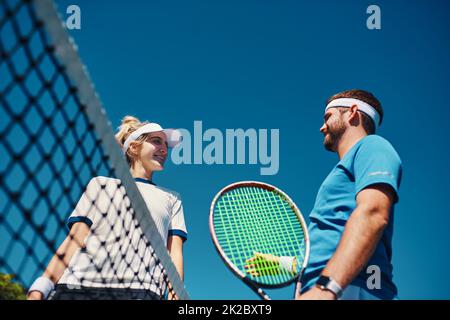 Vediamo che cosa hai ottenuto. Scatto ad angolo basso di due giovani giocatori di tennis che hanno una chiacchierata insieme all'aperto sul campo. Foto Stock