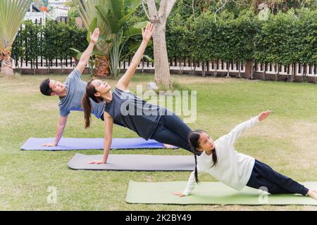 madre, padre che pratica le esercitazioni di yoga con la figlia del bambino all'aperto nella posa meditate insieme Foto Stock