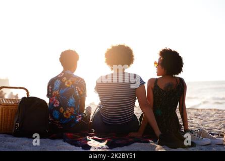 Gli amici sono quelli che fanno la vita degno vivere. Ripresa da dietro di un irriconoscibile trio di donne che hanno un picnic sulla spiaggia durante il giorno. Foto Stock