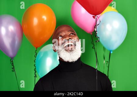 Vivete la vostra vita e siate allegri. Studio girato di un uomo in posa su uno sfondo verde con palloncini intorno a lui. Foto Stock