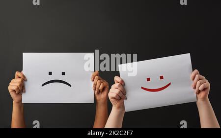 Felice e triste. Scatto di due persone che tengono un cartello con sorrisi felici e tristi su sfondo scuro. Foto Stock