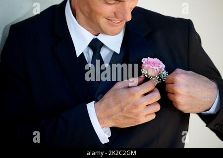 Questo è un bel tocco. Immagine ritagliata di uno sposo felice che regola il suo boutonniere prima che il matrimonio comincia. Foto Stock