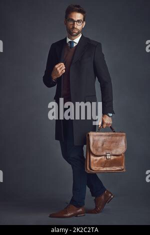 Stile thats buono per andare. Studio girato di un giovane uomo vestito con stile che porta una borsa su uno sfondo grigio. Foto Stock