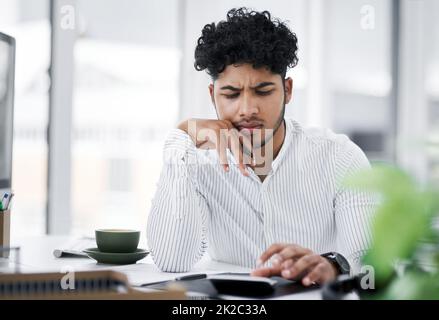 Avere alcuni problemi con il denaro conta. Scatto di un giovane uomo d'affari che osserva sottolineato fuori mentre usando una calcolatrice in un ufficio. Foto Stock