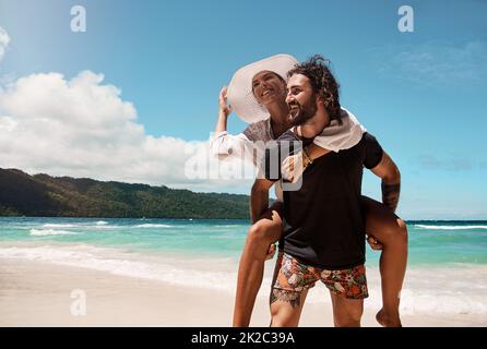 Avete bisogno di un ascensore. Scatto corto di una giovane coppia allegra che si danno a vicenda giri di piggyback mentre cammina su una spiaggia all'aperto durante il giorno. Foto Stock