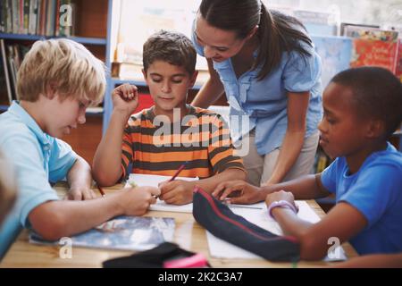 Mi piace la tua storia. Un insegnante piuttosto giovane che aiuta i suoi studenti con il loro lavoro in biblioteca. Foto Stock