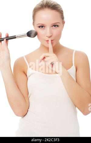 Questi sono i miei segreti di bellezza.... Una donna graziosa che mette un dito alle sue labbra mentre applica il rossore alla sua faccia. Foto Stock