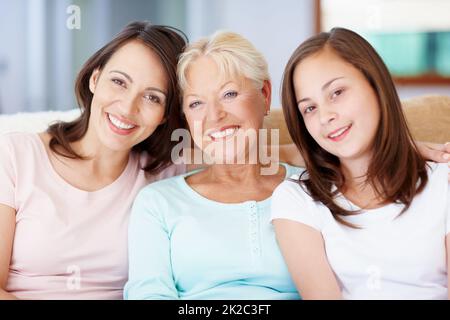 Granny, mamma e me. Tre generazioni di ragazze seduti insieme sul divano del salotto e sorridenti. Foto Stock