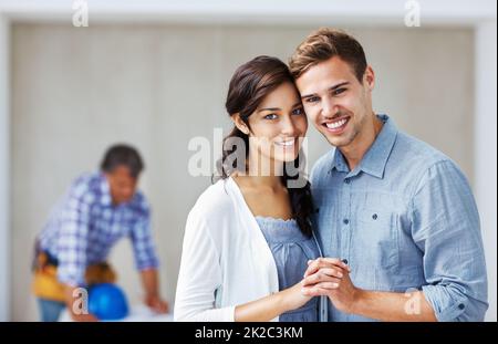 Felice coppia sorridente con architetto in background. Ritratto di giovane coppia amorevole sorridendo le mani con l'architetto sullo sfondo. Foto Stock