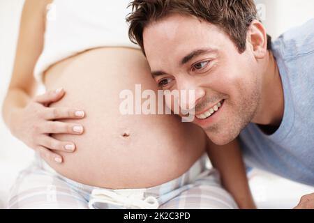 Eccitato per diventare un padre. Un uomo eccitato che ascolta il suo bambino che si muove nel suo stomaco del wifes. Foto Stock