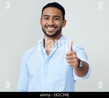 Continuate a fare quello che fate. Ritratto di un giovane uomo d'affari fiducioso che mostra i pollici su uno sfondo bianco. Foto Stock