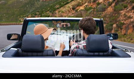 Penso che tu dovetti girarti qui Foto di una giovane coppia che legge una mappa mentre si siede in auto. Foto Stock