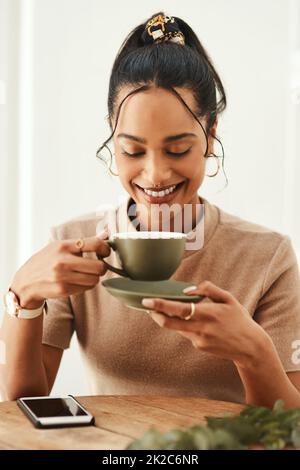 Questo buon umore è stato sponsorizzato dal caffè. Scatto corto di una giovane donna attraente seduta da sola nella sua casa e godendo una tazza di caffè. Foto Stock