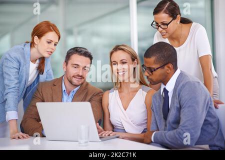 Mettendo le loro teste insieme. Girato di un gruppo diversificato di uomini d'affari che utilizzano un notebook insieme. Foto Stock