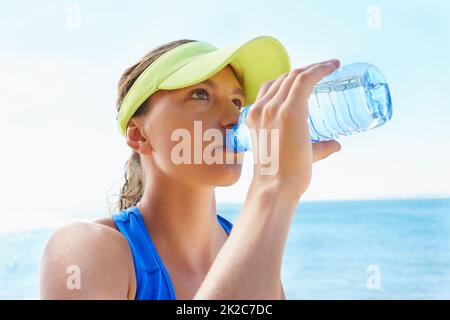 L'idratazione è fondamentale. Una giovane donna attraente e atletica che beve acqua dopo una corsa. Foto Stock