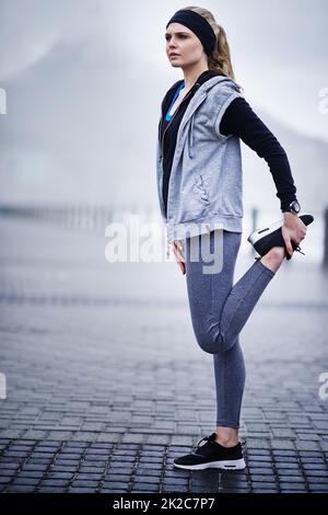 Motivati a mettersi in forma. Scatto di una giovane donna che allunga le gambe prima di una corsa. Foto Stock