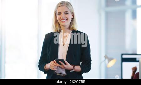 La fiducia è ciò di cui avete bisogno per far sopravvivere un'azienda. Ritratto di una giovane donna d'affari sicura che tiene il cellulare mentre si trova all'interno dell'ufficio. Foto Stock