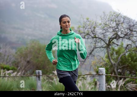 Progredisce nella sua idoneità giornaliere. Una giovane donna che si snoda lungo una strada di montagna in una mattinata frizzante. Foto Stock