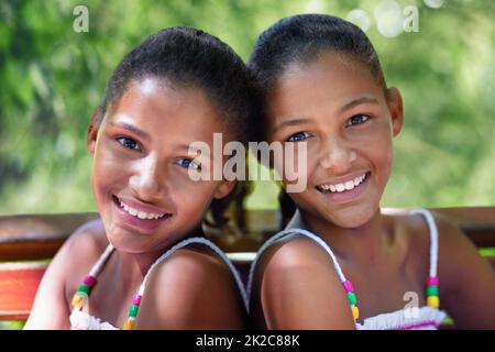 Due di un genere. Ritratto corto di due sorelle gemelle sedute su una panchina del parco. Foto Stock