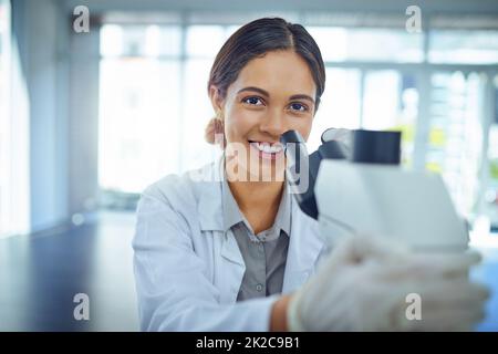 Shes un esperto a risolvere misteri scientifici. Ritratto di un giovane scienziato utilizzando un microscopio in un laboratorio. Foto Stock