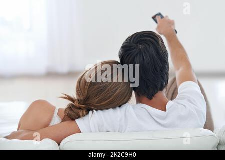 Canale hopping con la sua ragazza. Vista posteriore di una giovane coppia che guarda la TV insieme. Foto Stock