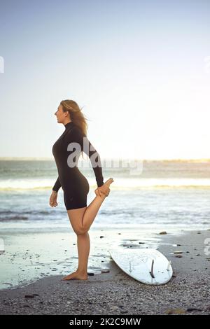 Limbering in su prima di colpire l'acqua. Profilo a tutta lunghezza girato di una giovane ragazza attraente surfer riscaldamento sulla spiaggia. Foto Stock