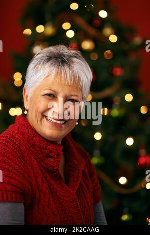 Sorride per babbo natale. Una donna felice e matura di fronte a un albero di Natale. Foto Stock