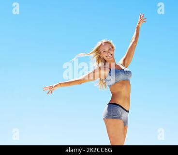 Perfetto come il tempo. Ritratto di una giovane donna in attrezzatura da allenamento in piedi contro un cielo blu. Foto Stock