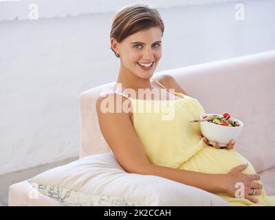 Il mio bambino merita la migliore nutrizione. Shot di una bella donna incinta che si rilassa sul divano mentre si mangia un'insalata fresca. Foto Stock