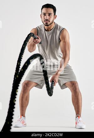 Anche il mio giorno peggiore, im ucciderlo. Studio girato di un giovane uomo muscolare esercitarsi con corde di battaglia su uno sfondo bianco. Foto Stock