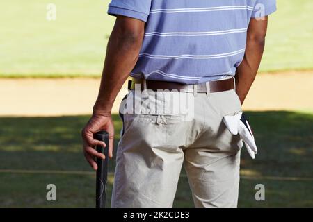 In attesa del suo tee-off. Dietro l'angolo corto di un golfista sezione centrale con un guanto appeso fuori dalla sua tasca posteriore. Foto Stock