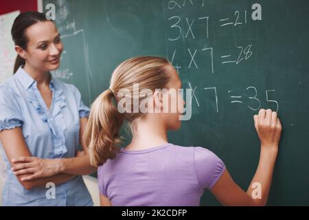 Migliorare la sua matematica. Un insegnante piuttosto giovane che aiuta la sua studentessa con un problema di matematica alla lavagna. Foto Stock