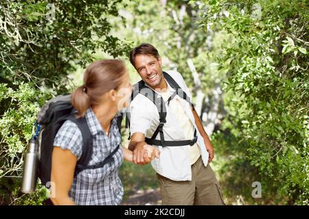Motivarsi a vicenda per continuare a muoversi. Un giovane che viene tirato giocosamente dalla moglie con zaini sulle spalle. Foto Stock